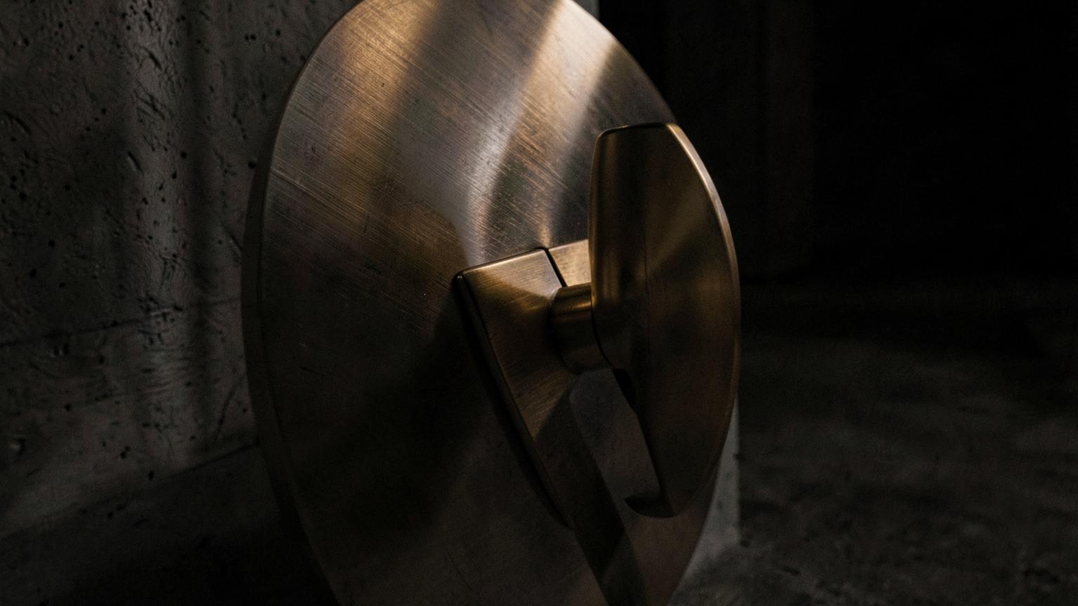 Close view of a brushed steel vault door with a brass handle in low light